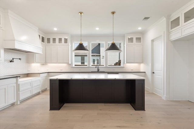 kitchen with white cabinetry, custom exhaust hood, light wood-type flooring, a kitchen island, and pendant lighting