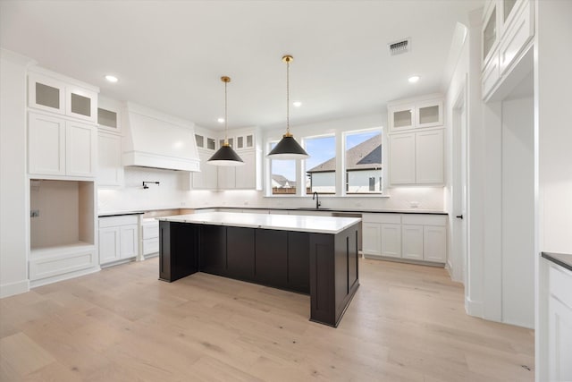 kitchen with decorative light fixtures, white cabinets, light wood-type flooring, and a kitchen island