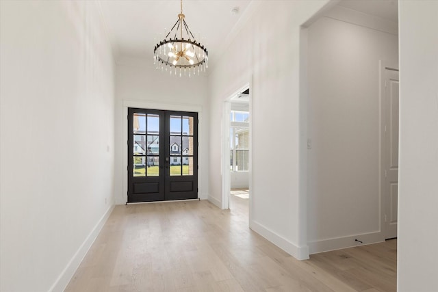 foyer featuring light wood-type flooring, french doors, an inviting chandelier, and ornamental molding