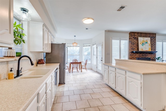 kitchen featuring light tile patterned floors, a brick fireplace, hanging light fixtures, white cabinets, and sink