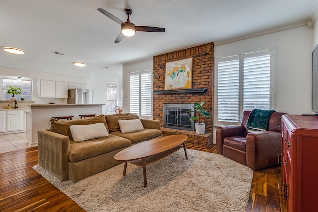 living room featuring ceiling fan, crown molding, a fireplace, and wood-type flooring