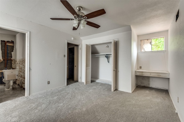 unfurnished bedroom with ceiling fan, a textured ceiling, ensuite bathroom, and light carpet