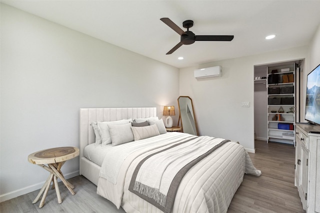 bedroom with an AC wall unit, baseboards, light wood-type flooring, and recessed lighting