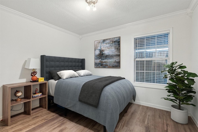 bedroom featuring crown molding, baseboards, a textured ceiling, and wood finished floors