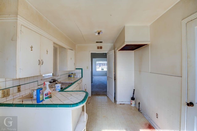 kitchen with white cabinetry, decorative backsplash, sink, kitchen peninsula, and tile countertops