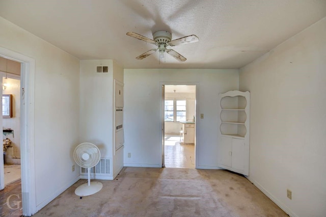 empty room featuring ceiling fan, a textured ceiling, and light carpet