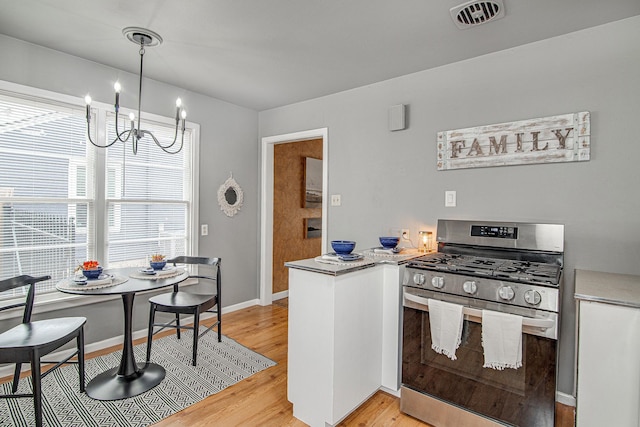 kitchen featuring a notable chandelier, pendant lighting, stainless steel range with gas stovetop, white cabinetry, and light wood-type flooring