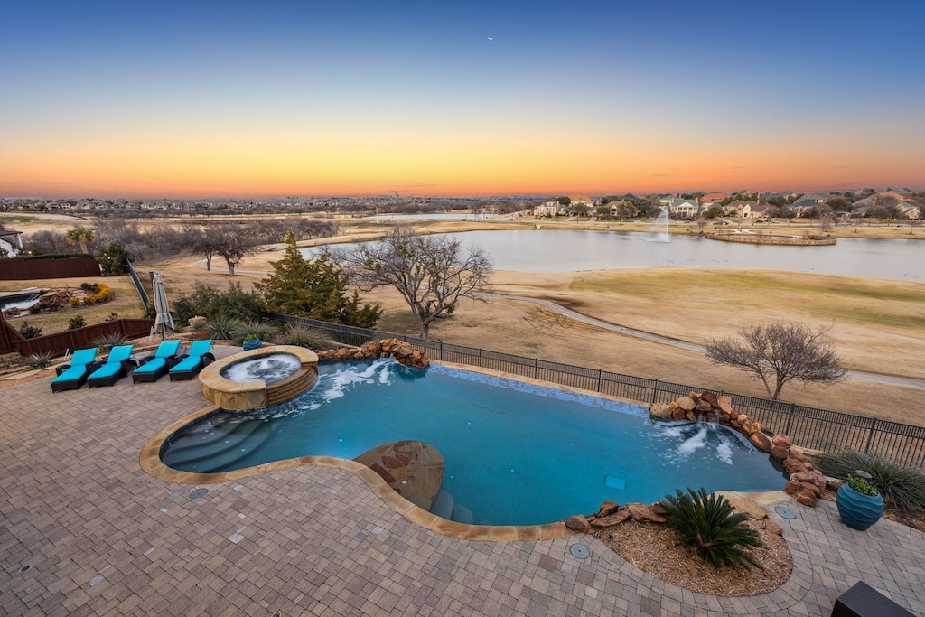 pool at dusk with pool water feature, a patio area, and a water view