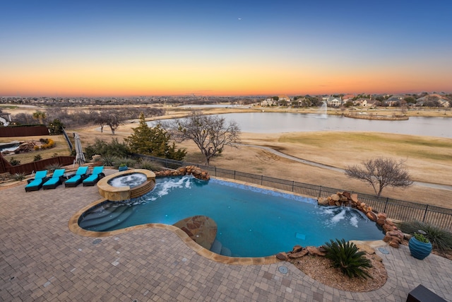 pool at dusk with pool water feature, a water view, and a patio