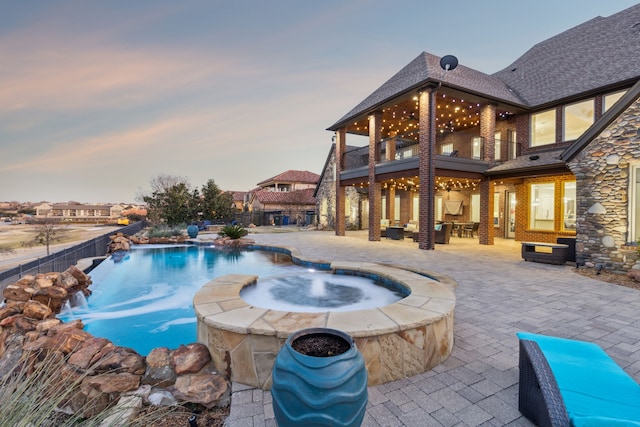 pool at dusk featuring pool water feature, a patio area, and an in ground hot tub