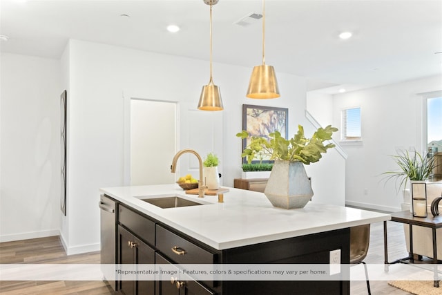 kitchen featuring dishwasher, sink, hanging light fixtures, a kitchen island with sink, and light wood-type flooring