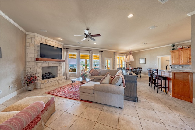 living room featuring a textured ceiling, a fireplace, ceiling fan, light tile patterned floors, and crown molding