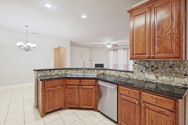 kitchen with ceiling fan with notable chandelier, decorative light fixtures, dark stone counters, sink, and stainless steel dishwasher