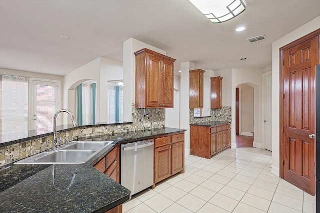 kitchen featuring stainless steel dishwasher, dark stone counters, tasteful backsplash, sink, and light tile patterned floors