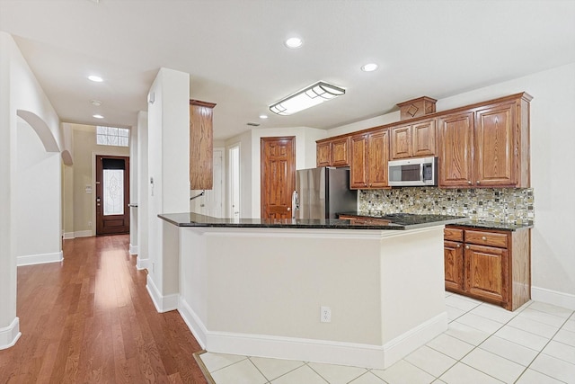 kitchen featuring kitchen peninsula, appliances with stainless steel finishes, tasteful backsplash, dark stone countertops, and light hardwood / wood-style flooring