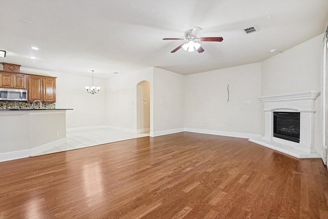 unfurnished living room featuring ceiling fan with notable chandelier and wood-type flooring