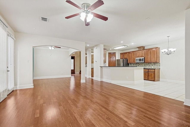 unfurnished living room featuring light wood-type flooring and ceiling fan with notable chandelier