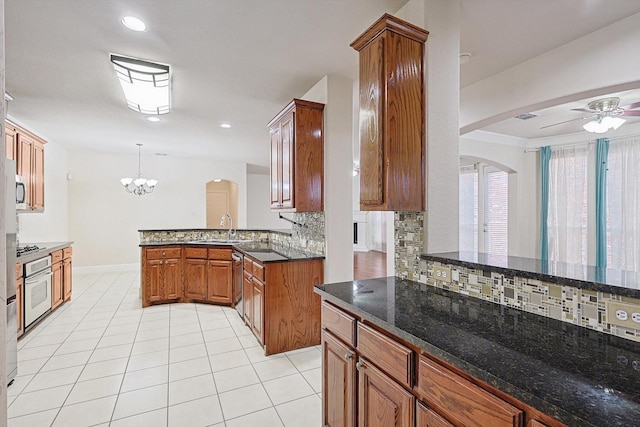 kitchen with kitchen peninsula, stainless steel appliances, backsplash, hanging light fixtures, and ceiling fan with notable chandelier