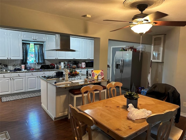 kitchen featuring stainless steel refrigerator with ice dispenser, a center island, dark stone countertops, wall chimney range hood, and white cabinets