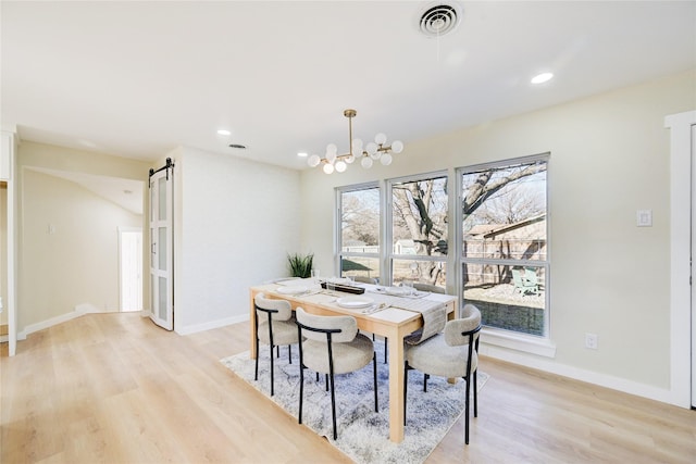 dining area with plenty of natural light, a barn door, light hardwood / wood-style flooring, and a notable chandelier