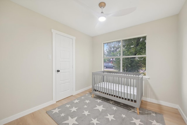 bedroom with hardwood / wood-style floors, a crib, and ceiling fan