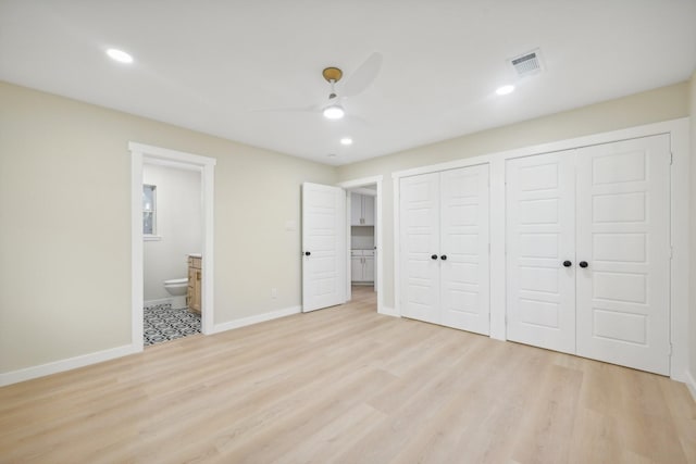 unfurnished bedroom with ceiling fan, two closets, connected bathroom, and light wood-type flooring