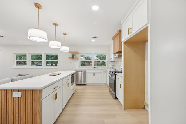 kitchen with white cabinetry, stainless steel appliances, a healthy amount of sunlight, a kitchen island, and decorative light fixtures