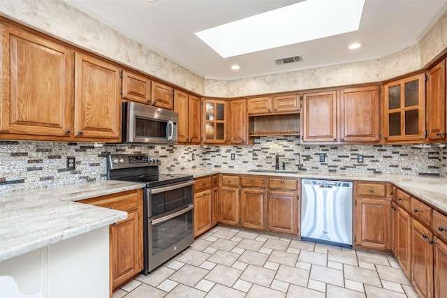 kitchen with light stone countertops, a skylight, stainless steel appliances, and sink