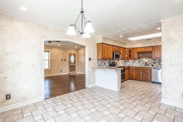 kitchen with tasteful backsplash, kitchen peninsula, crown molding, hanging light fixtures, and stainless steel appliances