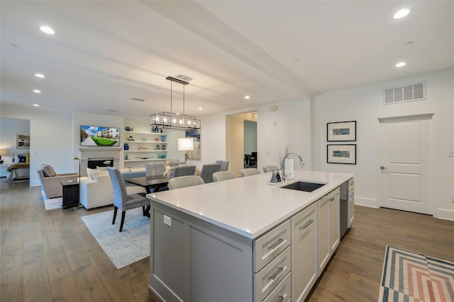 kitchen with sink, dark wood-type flooring, hanging light fixtures, and a center island with sink