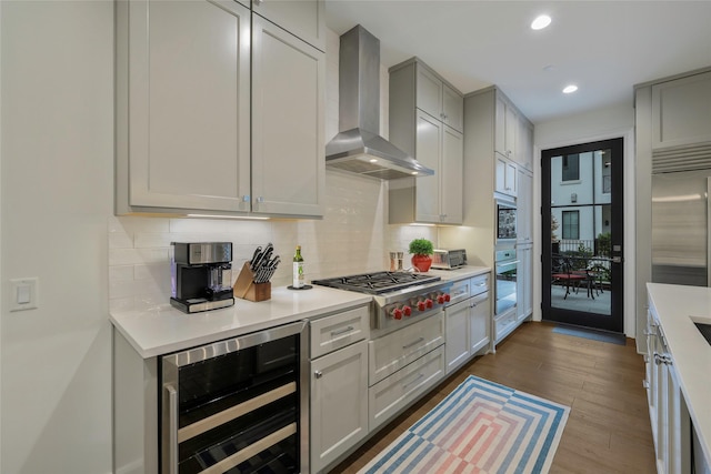 kitchen featuring wall chimney range hood, appliances with stainless steel finishes, hardwood / wood-style floors, wine cooler, and tasteful backsplash