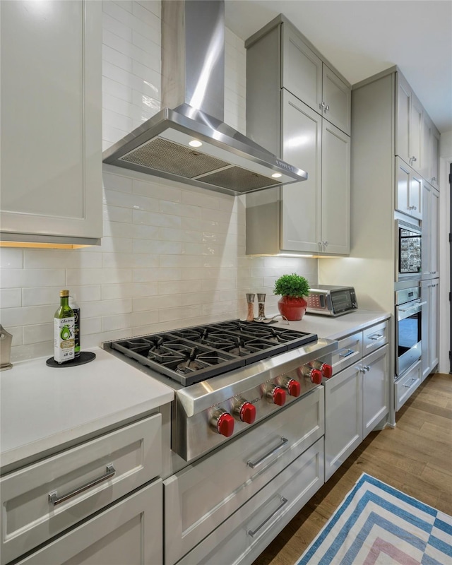 kitchen with gray cabinets, appliances with stainless steel finishes, backsplash, dark hardwood / wood-style flooring, and wall chimney range hood