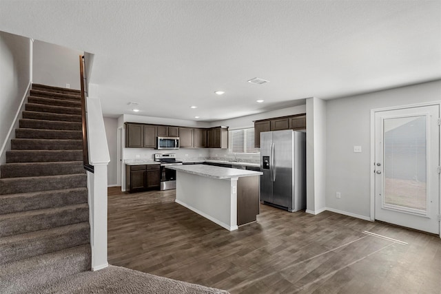 kitchen featuring appliances with stainless steel finishes, dark hardwood / wood-style flooring, a kitchen island, dark brown cabinetry, and sink