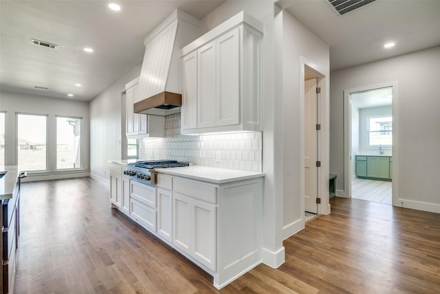 kitchen with backsplash, custom exhaust hood, light hardwood / wood-style flooring, stainless steel gas cooktop, and white cabinets