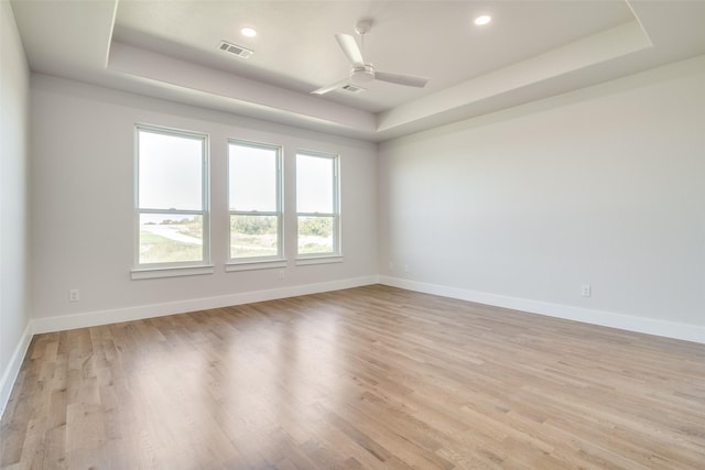 spare room with ceiling fan, a tray ceiling, and light hardwood / wood-style flooring