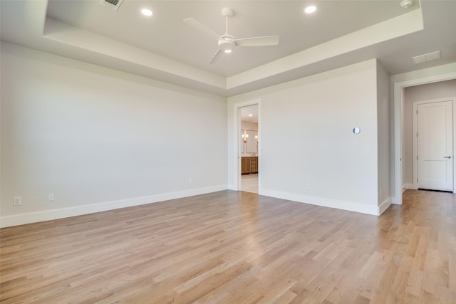 unfurnished room featuring ceiling fan, light hardwood / wood-style flooring, and a raised ceiling