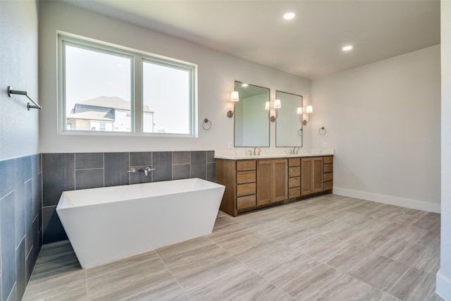 bathroom with a tub to relax in, vanity, tile walls, and tile patterned floors