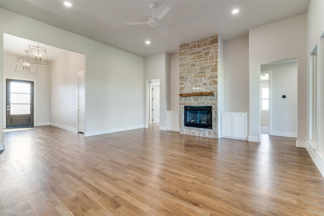 unfurnished living room with ceiling fan with notable chandelier, a stone fireplace, and light wood-type flooring