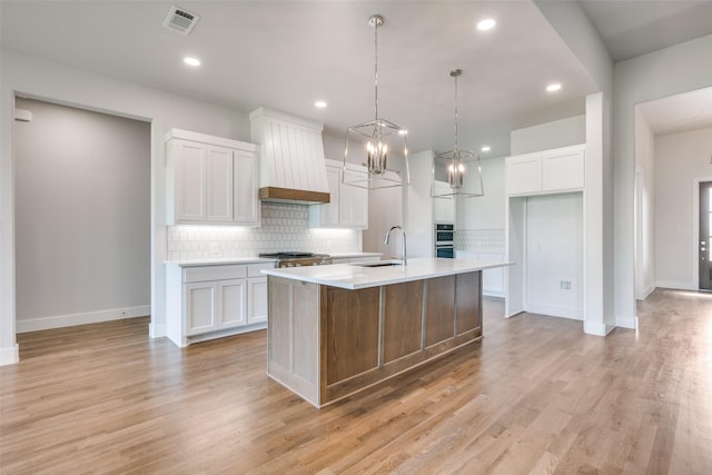 kitchen featuring light hardwood / wood-style floors, a center island with sink, sink, white cabinetry, and custom range hood