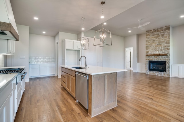 kitchen featuring pendant lighting, white cabinets, sink, stainless steel dishwasher, and a center island with sink