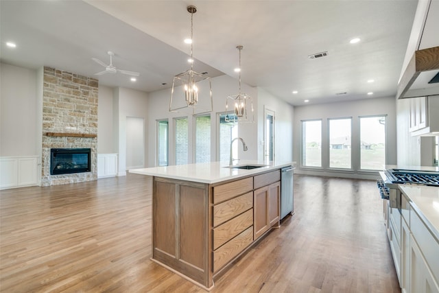 kitchen featuring a stone fireplace, an island with sink, stainless steel appliances, light wood-type flooring, and sink