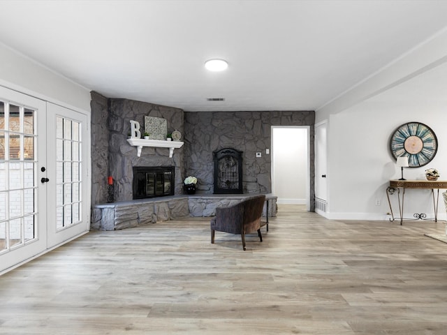 living room with light hardwood / wood-style floors, french doors, and a stone fireplace