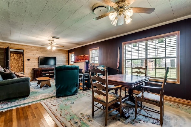 dining area featuring ceiling fan, crown molding, hardwood / wood-style floors, and wooden walls