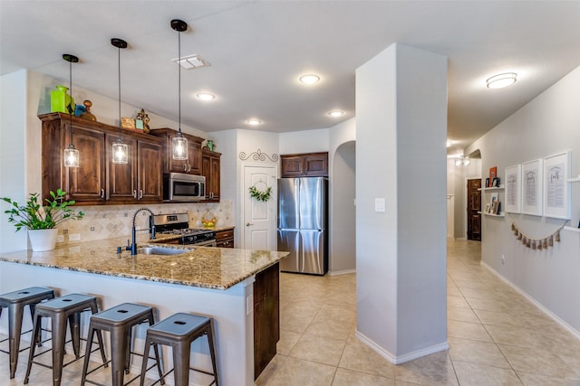 kitchen featuring kitchen peninsula, stainless steel appliances, backsplash, decorative light fixtures, and sink