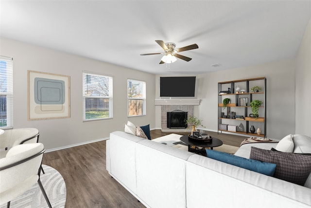 living room with a brick fireplace, dark wood-type flooring, and ceiling fan