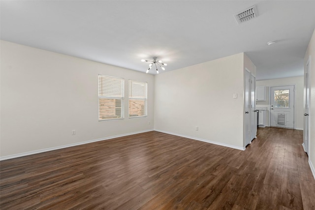 empty room with dark wood-type flooring and a chandelier