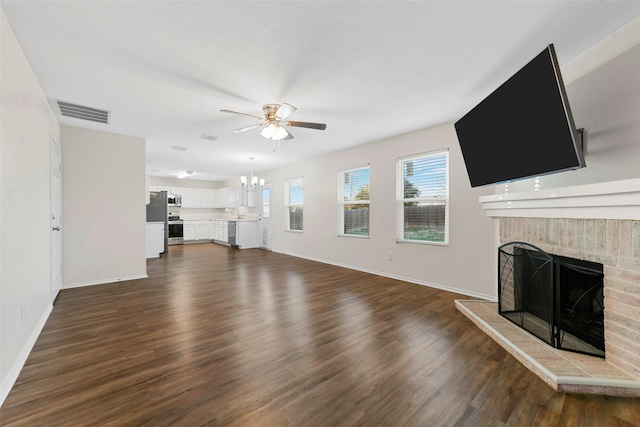 unfurnished living room with a brick fireplace, dark hardwood / wood-style flooring, and ceiling fan with notable chandelier