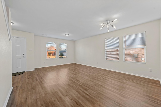 empty room featuring wood-type flooring and an inviting chandelier