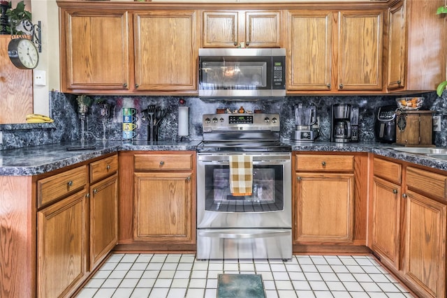 kitchen featuring light tile patterned floors, appliances with stainless steel finishes, dark stone counters, and tasteful backsplash