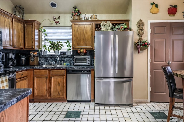 kitchen with stainless steel appliances, dark stone countertops, sink, backsplash, and light tile patterned floors